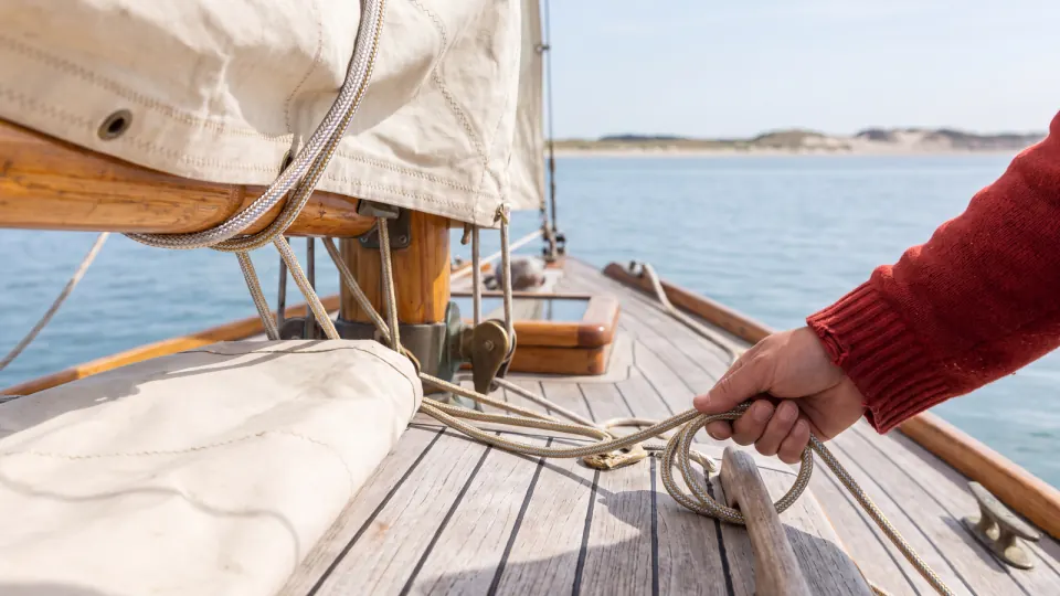 Hand auf dem Deck einer Segelyacht, dahinter Segeltuch und ruhiges Meer