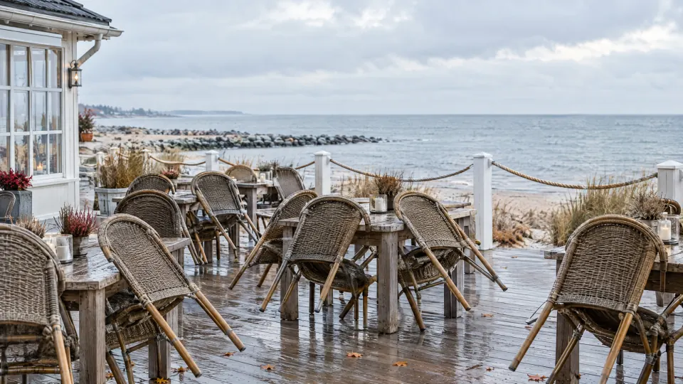 Leere Restaurantterrasse an der Küste im Herbst, gekippte Korbstühle auf nassem Holzboden