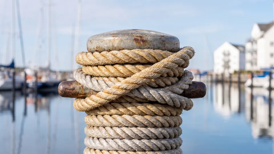 Festmacherleine um einen Poller im Yachthafen, im Hintergrund unscharfe Masten