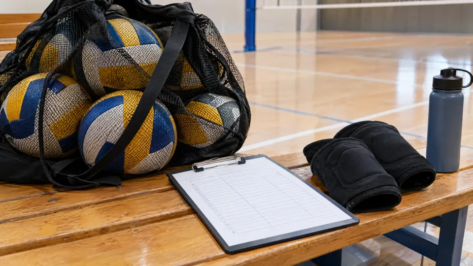 Hallenbank mit einem Netz voller Volleybälle, Klemmbrett mit Mannschaftsliste, Knieschonern und Trinkflasche