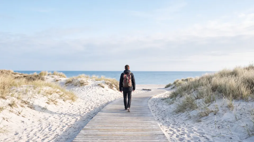 Holzsteg durch die Dünen zur Ostsee, eine Person mit Rucksack geht von hinten gesehen Richtung Meer