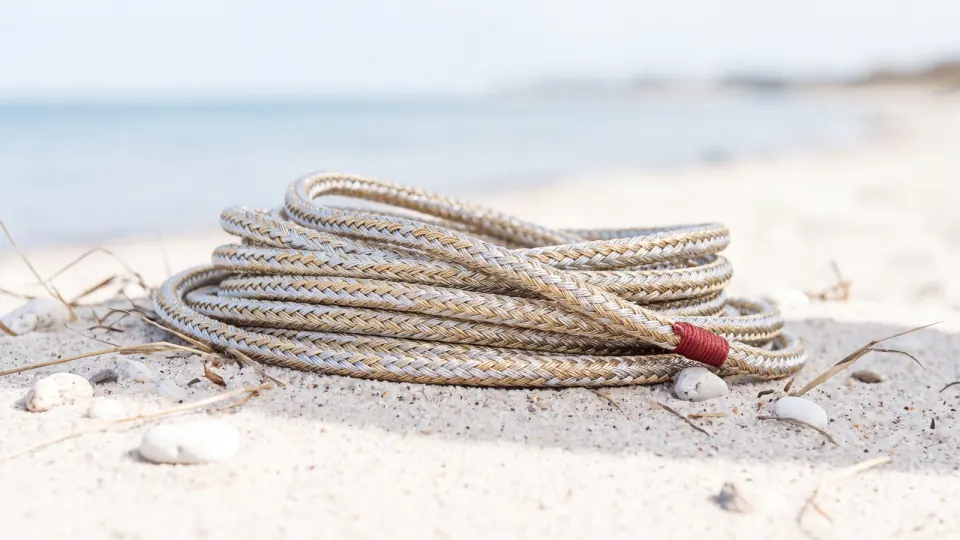 Sauber gelegtes Tau in Silber- und Goldtönen auf hellem Sand