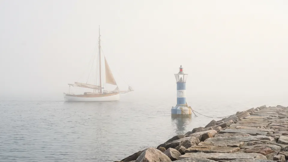 Hafeneinfahrt im dichten Nebel mit Segelboot und Seezeichen