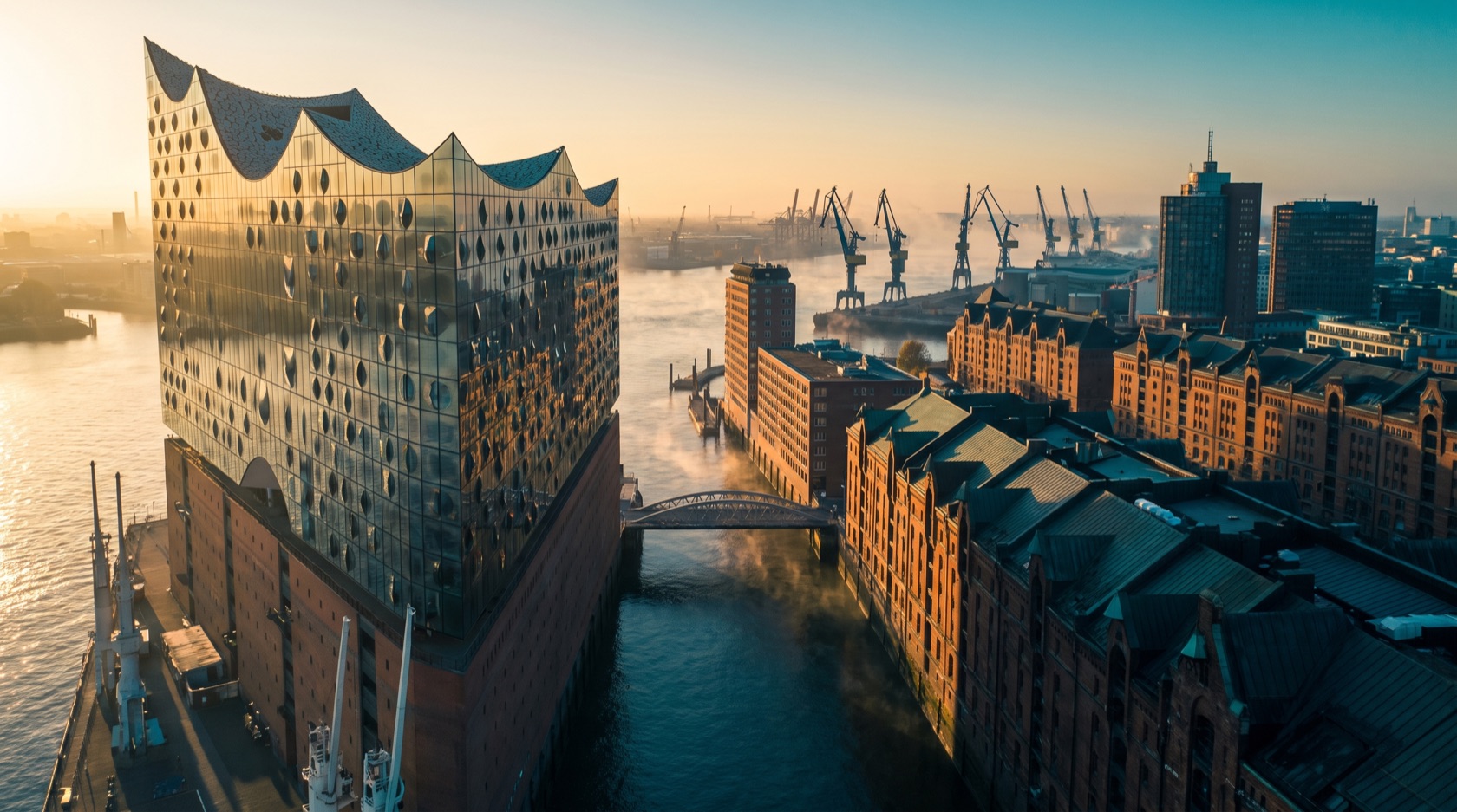 Hamburg bei Abenddämmerung: die Elbphilharmonie an der HafenCity, die Backstein-Speicherstadt und die Kräne des größten Hafens Deutschlands